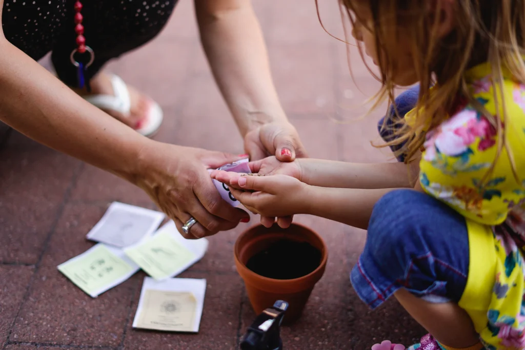 Adult helping child to plant seeds in pot