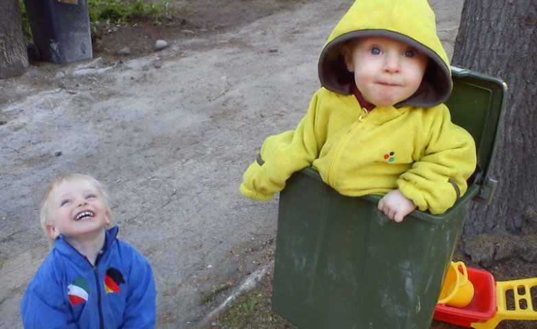 pieni lapsi on ulkona postilaatikossa ja katsoo kameraan, toinen nauraa iloisesti